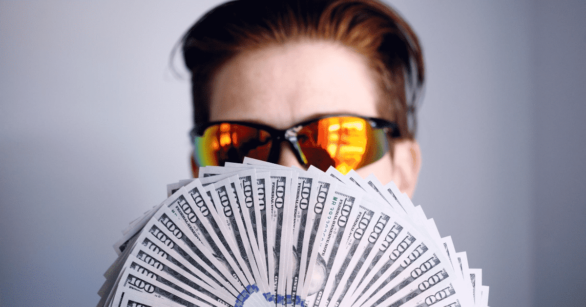 A person with sunglasses holding 100 dollar bills